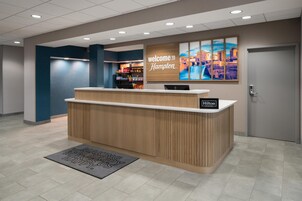 Un mostrador de recepción de hotel con un cartel que dice 'Welcome to Hampton', una pantalla digital y vistas de la ciudad.