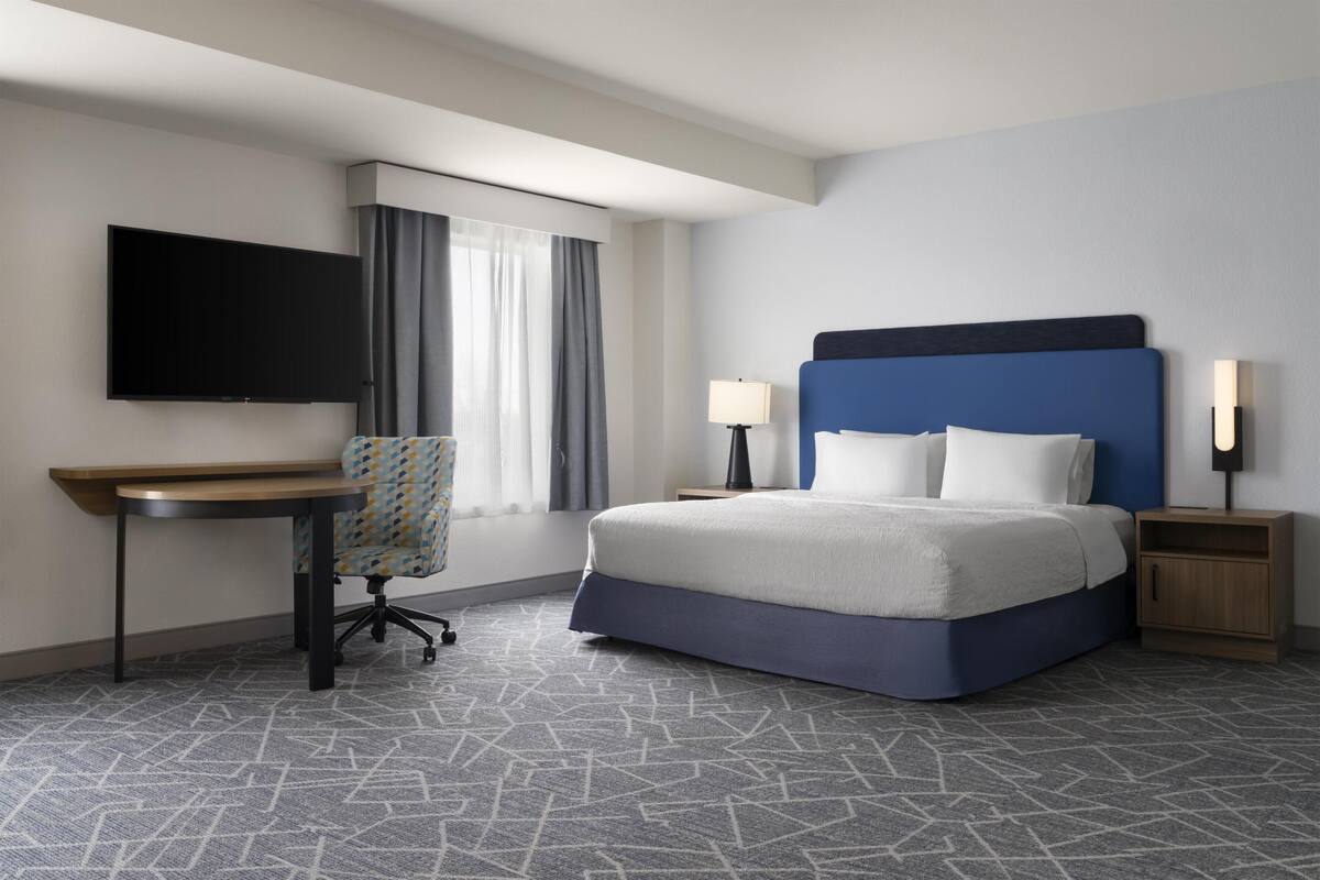 A hotel room with a bed, a desk, a chair, a TV, and a nightstand.