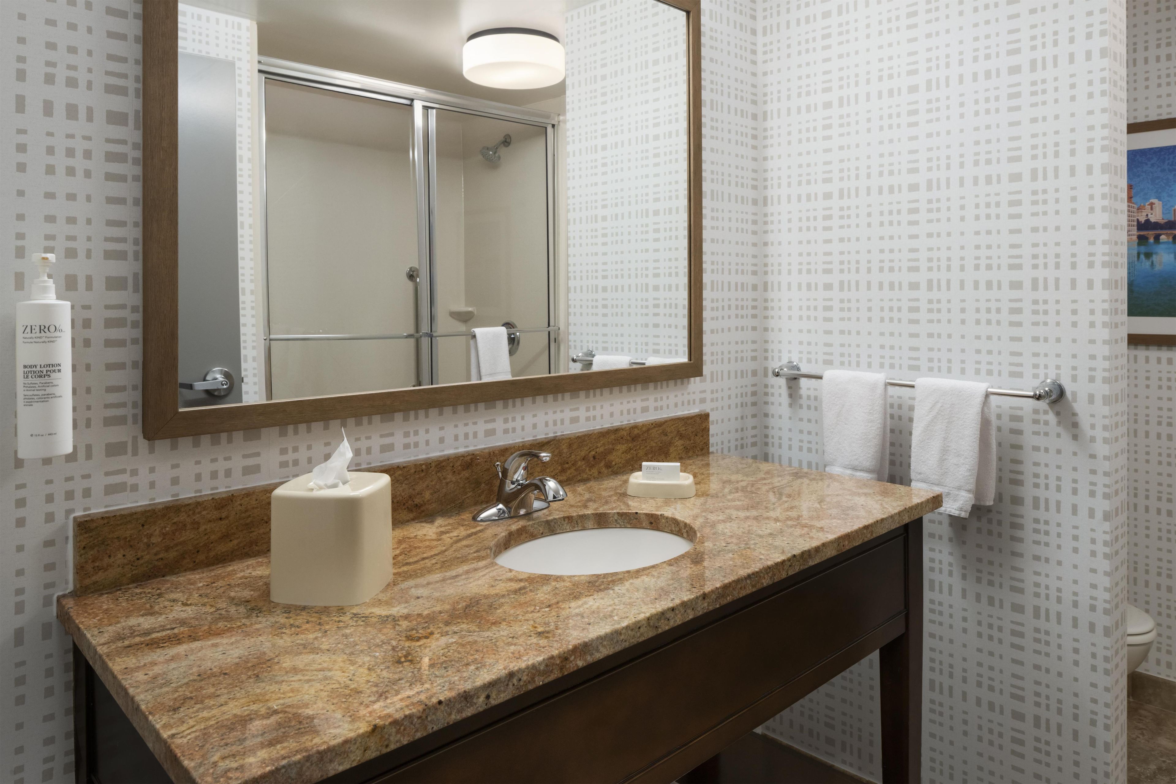A bathroom with a marble sink, a mirror, a towel rack, and a bottle of body lotion.