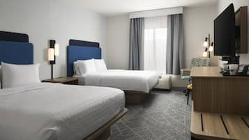 A hotel room with two beds, a desk, a television, and a window with curtains.