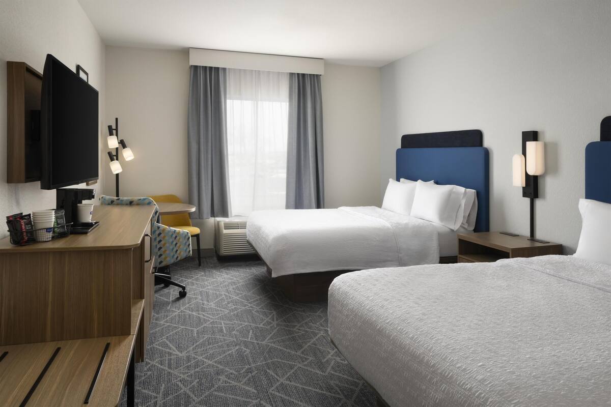 A hotel room with two beds, a desk, a television, and a window with curtains.