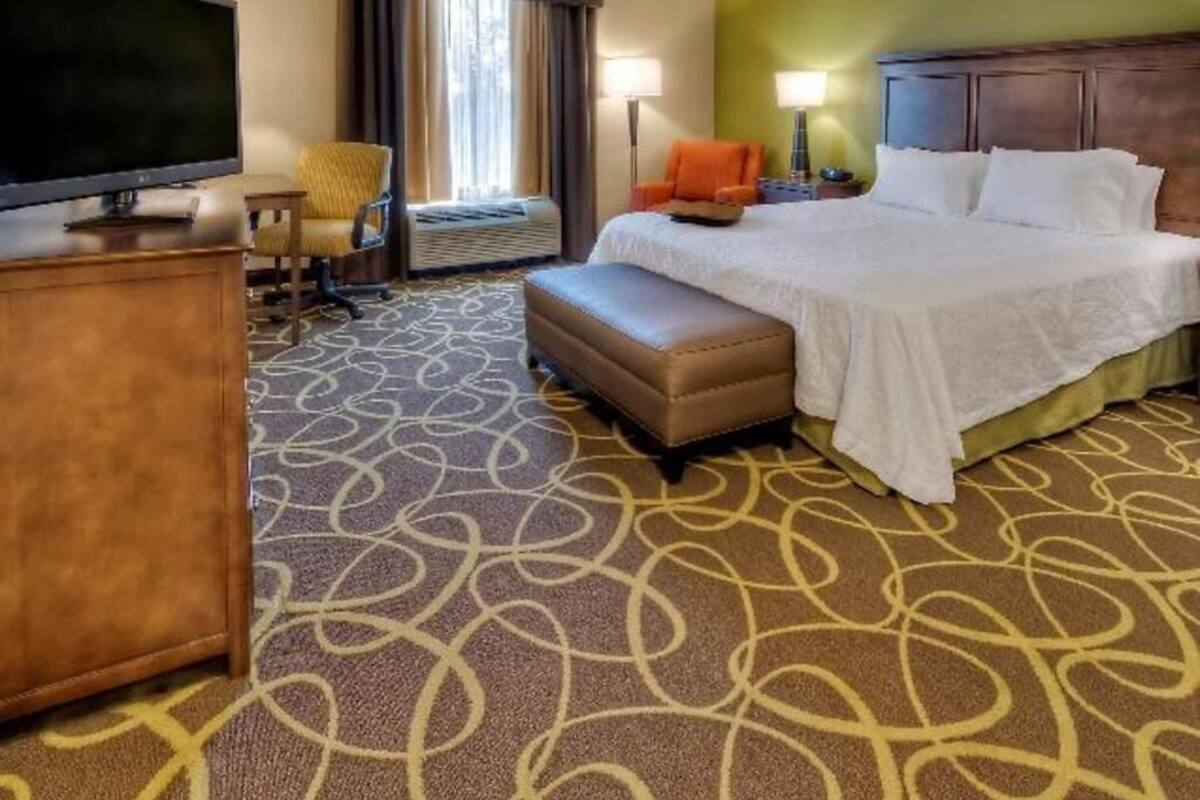 A hotel room with a bed, a television, a desk, a chair, and an air conditioning unit.