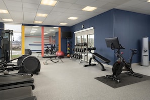 Een fitnessruimte met diverse trainingsapparaten, waaronder loopbanden, hometrainers en gewichten.
