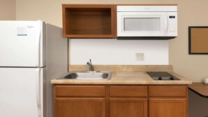 Une cuisine compacte équipée d’un réfrigérateur, d’un four à micro-ondes, d’un évier et de meubles de rangement en bois.