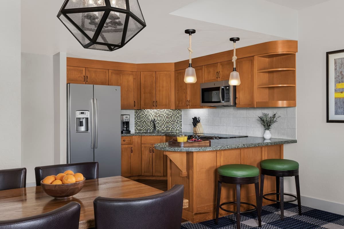 A modern kitchen with wooden cabinets, a stainless steel refrigerator, a microwave, and a built-in island with bar stools.