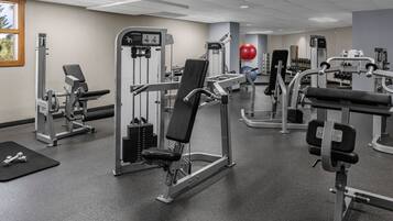 Een sportschool met diverse fitnessapparaten, een rode trainingsbal en gewichten.