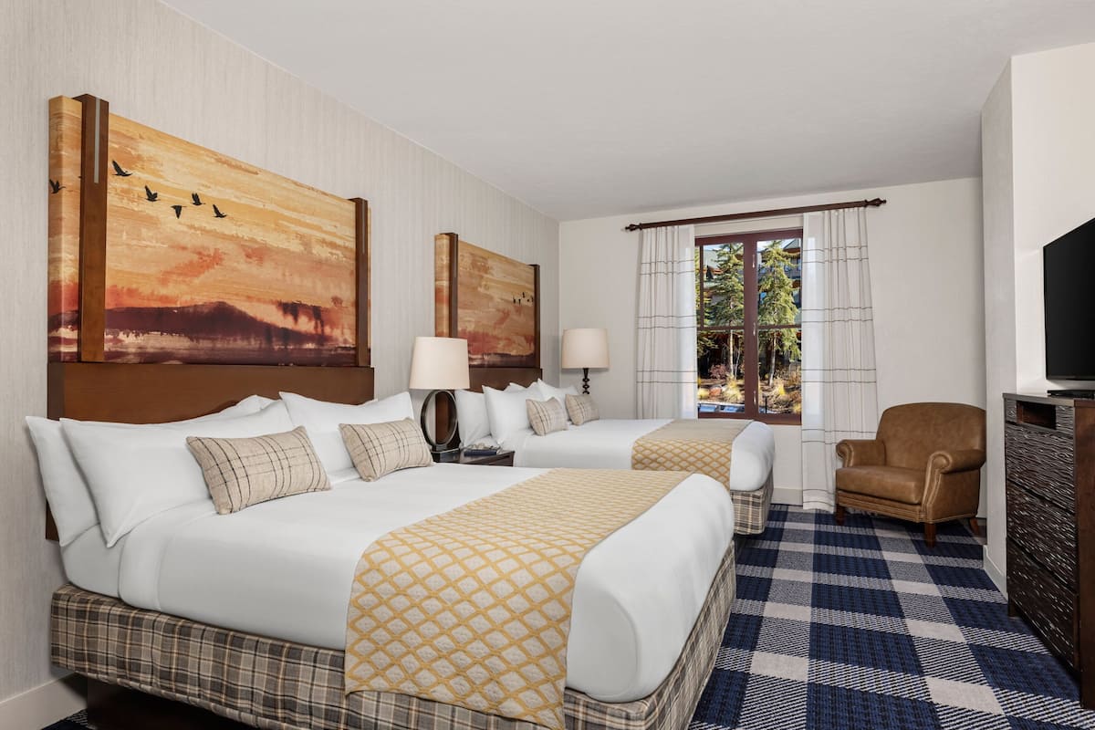 A hotel room with two beds, a television, a chair, and artwork on the walls.