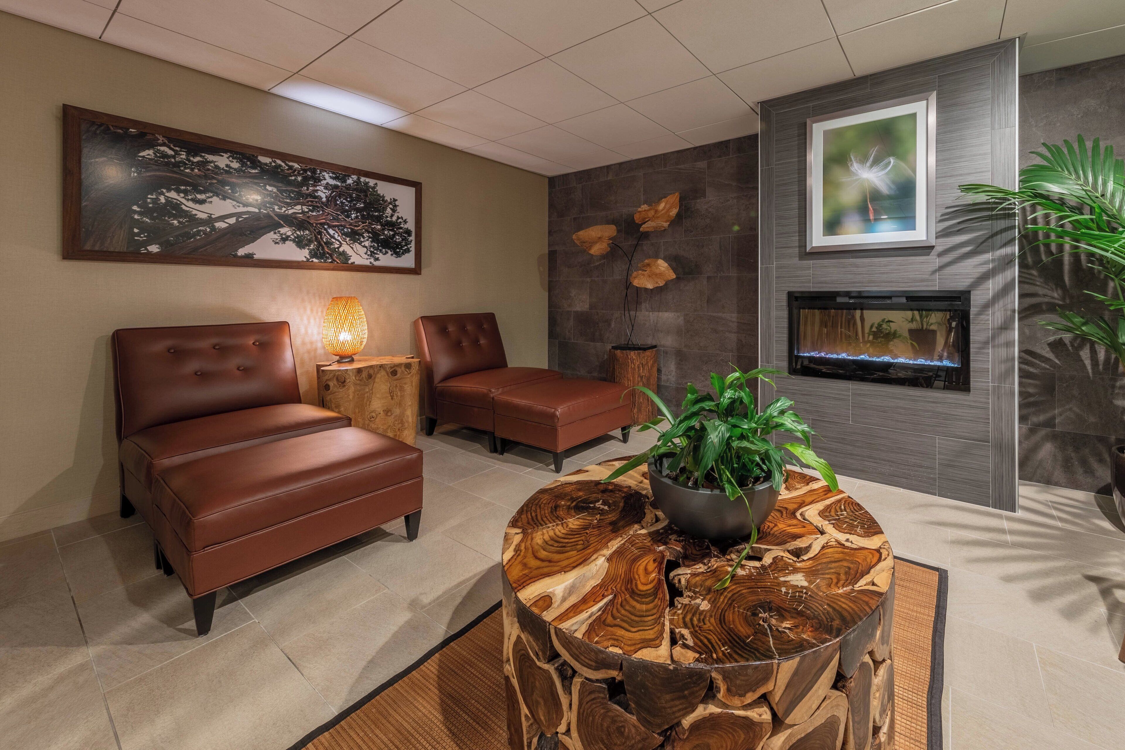 Un espacio lounge moderno con un sofá de cuero marrón, una mesa de centro de madera con una planta y una chimenea.