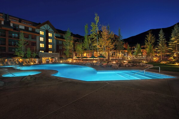 A large outdoor swimming pool with multiple sections, surrounded by lounge chairs and umbrellas, and adjacent to a multi-story building with illuminated windows. - Marriott Grand Residence Club, Lake Tahoe – 1 to 3 bedrooms & Pent (South Lake Tahoe)