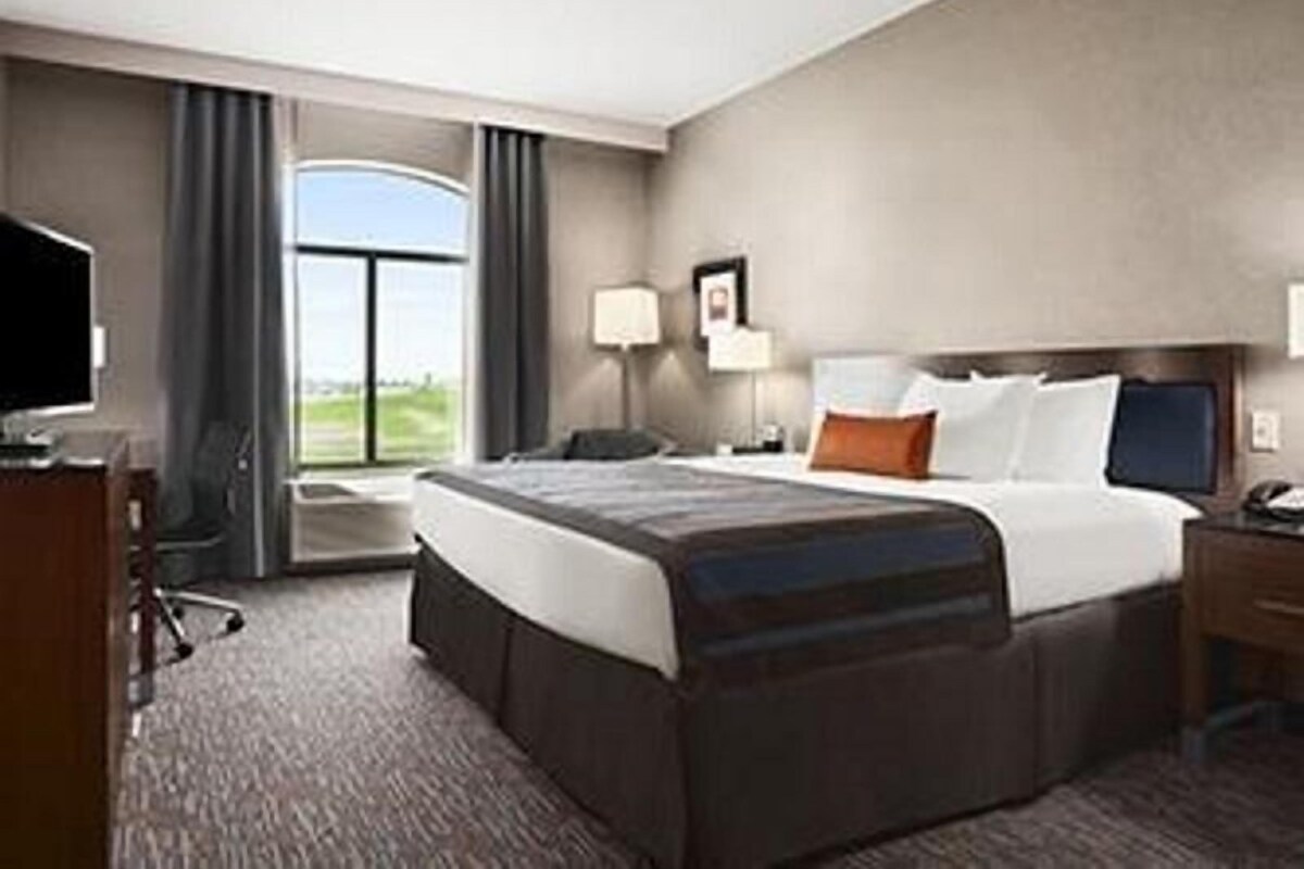 Ein Hotelzimmer mit Bett, Schreibtisch, Stuhl, Fernseher, Fenster und Lampe.