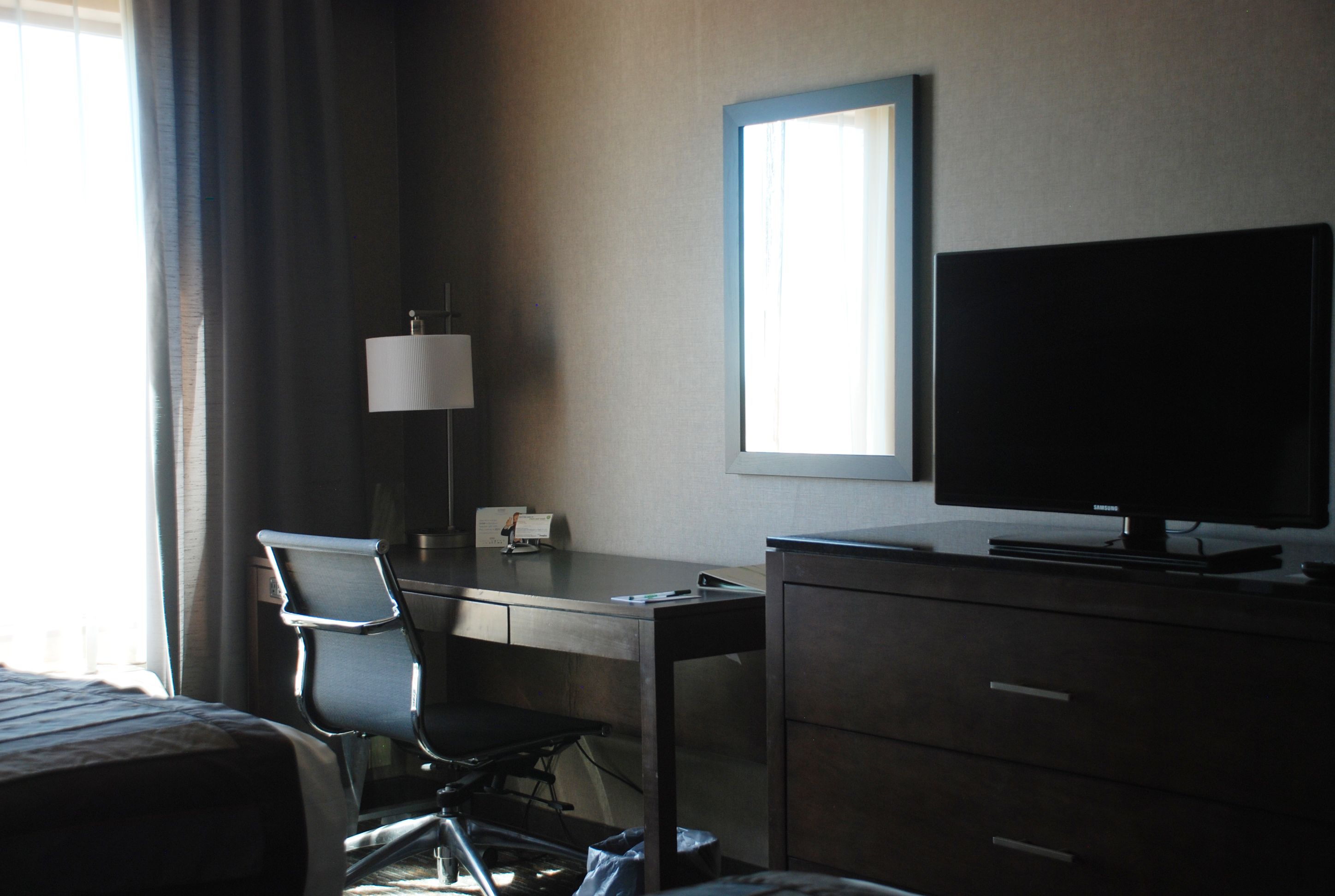 A hotel room with a bed, a desk, a chair, a television, and a window.