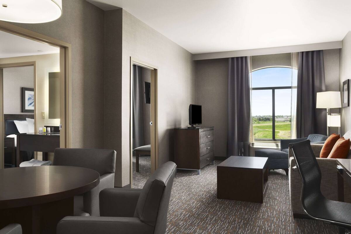 Une chambre d’hôtel moderne dotée d’un coin repas, d’un canapé, d’une télévision et offrant une vue sur l’extérieur.