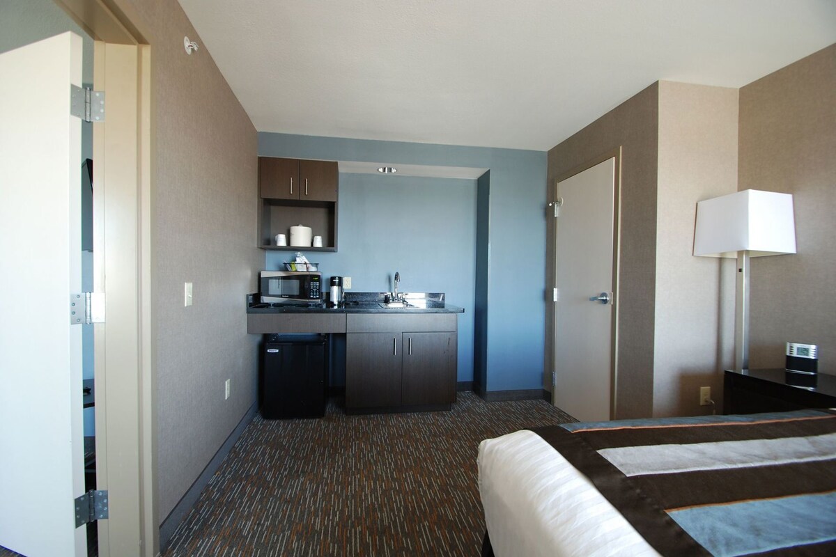 Ein Hotelzimmer mit Küchenzeile, einem Bett, einem Schreibtisch und einer Lampe.