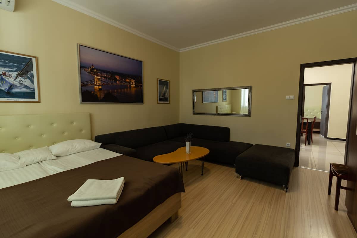 Ein Hotelzimmer mit Bett, Sofa, kleinem Tisch und Spiegel. An der Wand hängen zwei Gemälde.
