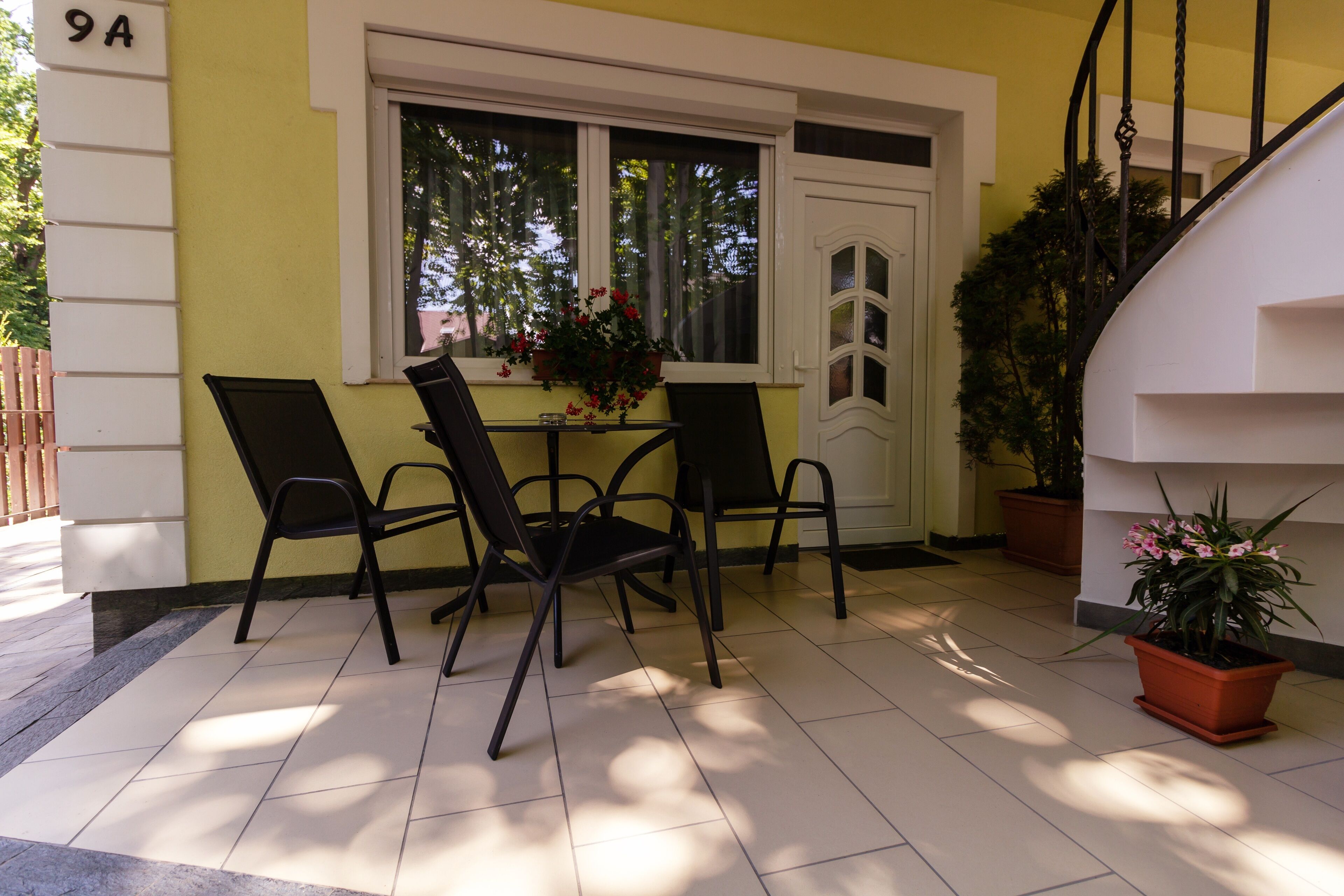 Un patio con una mesa y sillas, una ventana adornada con plantas en macetas y una puerta.