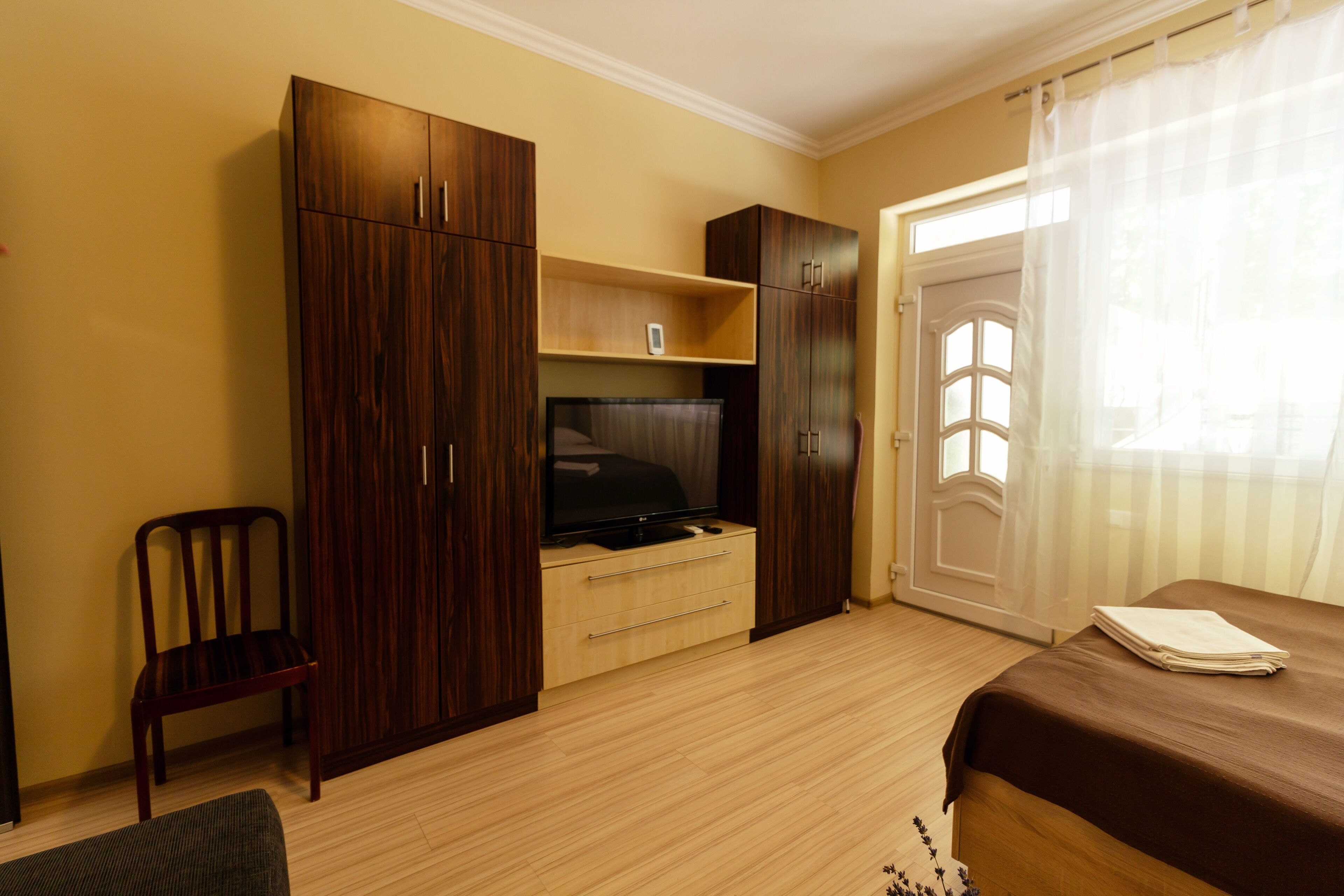 A bedroom with a bed, a TV, wooden wardrobe, and a chair.
