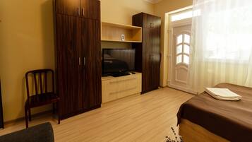 A bedroom with a bed, a TV, wooden wardrobe, and a chair.