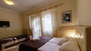 A hotel room with a bed, a sofa bed, a flat-screen TV mounted on the wall, and a painting on the wall. - Bella Villa Siofok (Siófok)