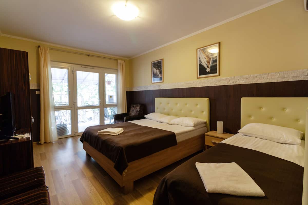 Ein Hotelzimmer mit zwei Betten, einem Fernseher, einem Sessel und einem Fenster mit Vorhängen.