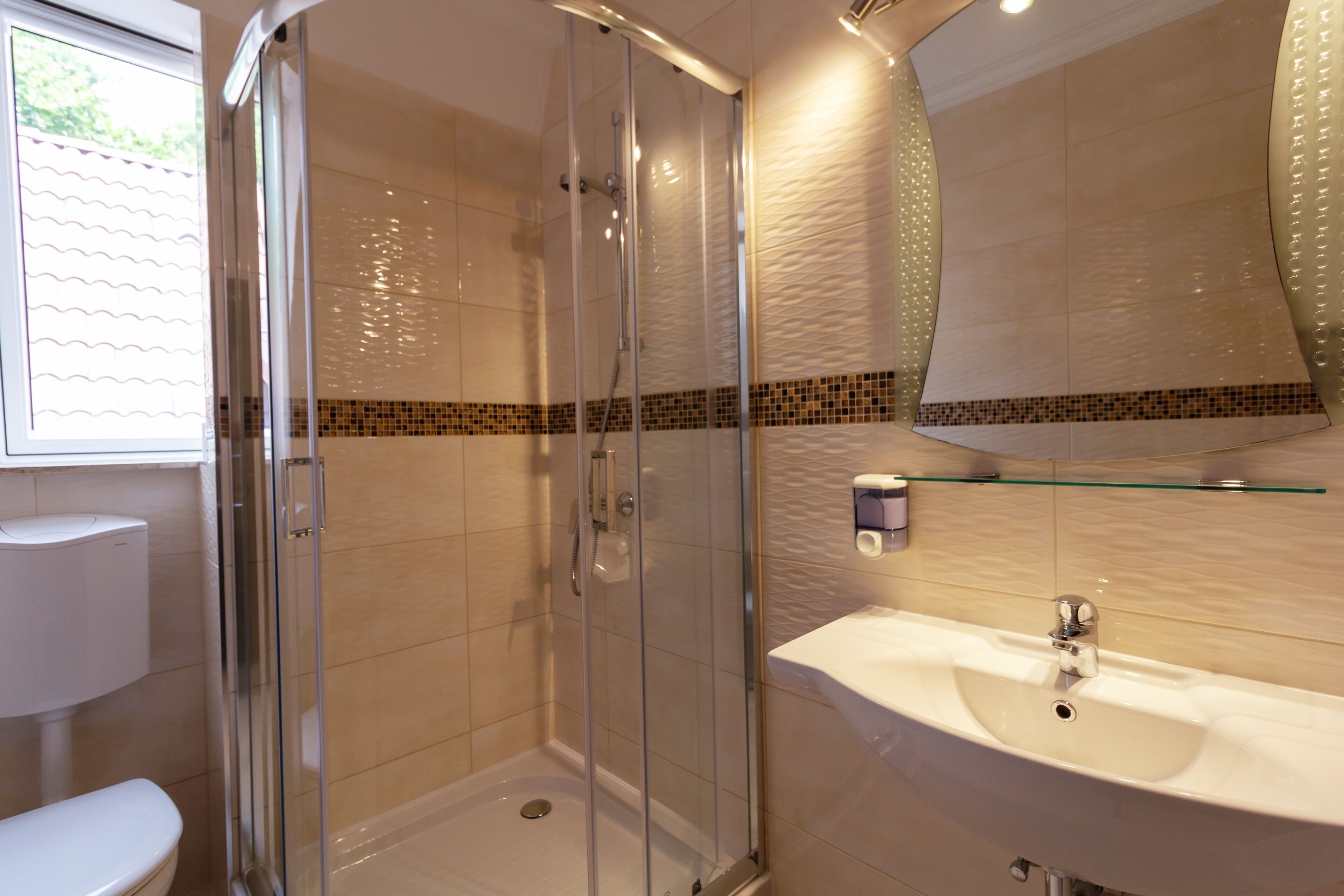 A modern bathroom with a glass-enclosed shower, a white sink, and a tiled backsplash.