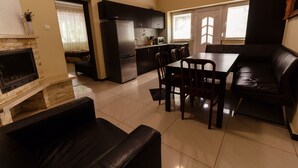 A modern kitchen with dark cabinets, a dining area with a table and chairs, and a fireplace. - Bella Villa Siofok (Siófok)