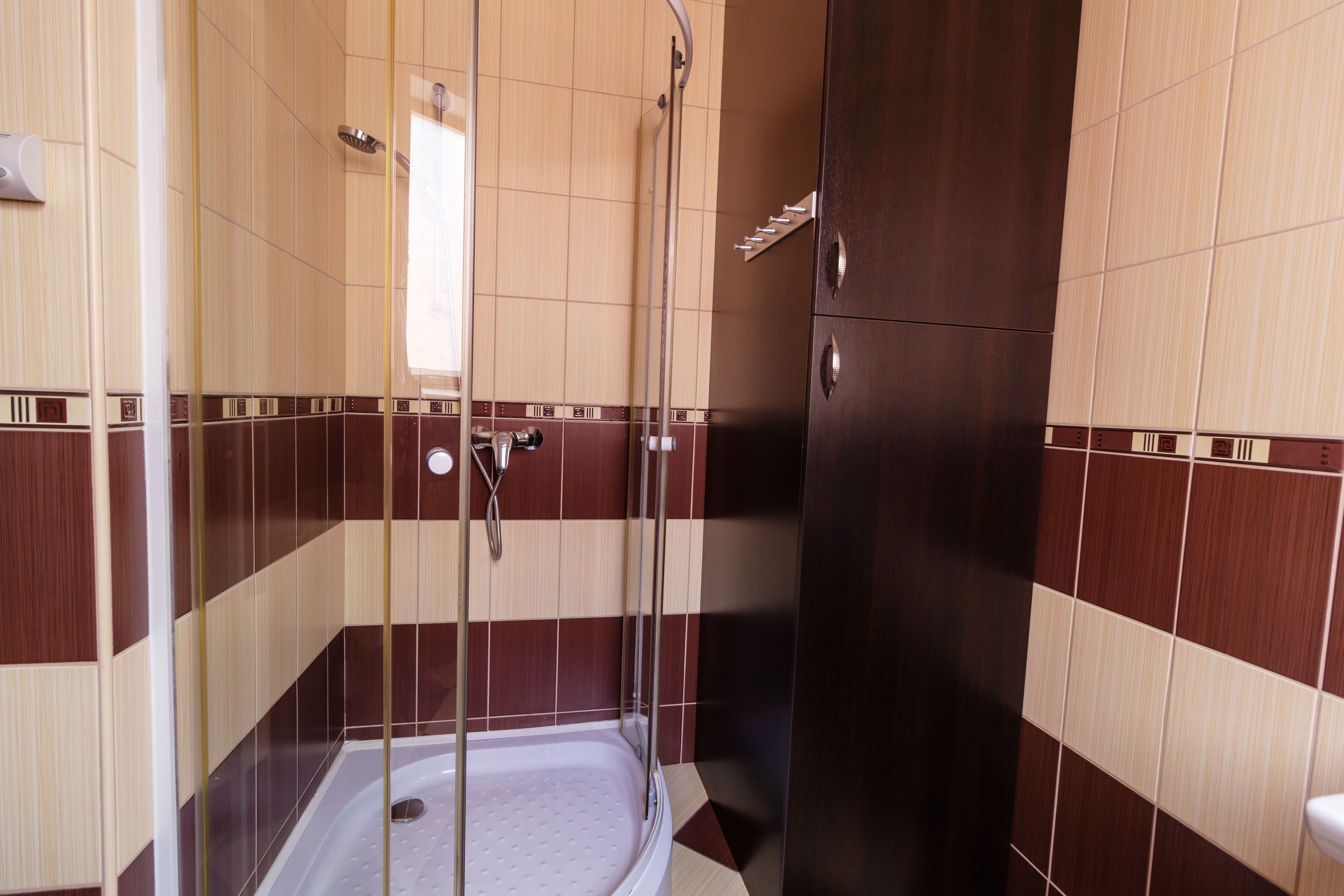 A shower area with a glass door, a handheld showerhead, and a wall-mounted faucet.