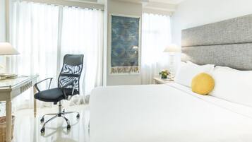 Habitación de hotel con una cama grande, un escritorio con silla, una mesita de noche con lámpara y una obra de arte en la pared.