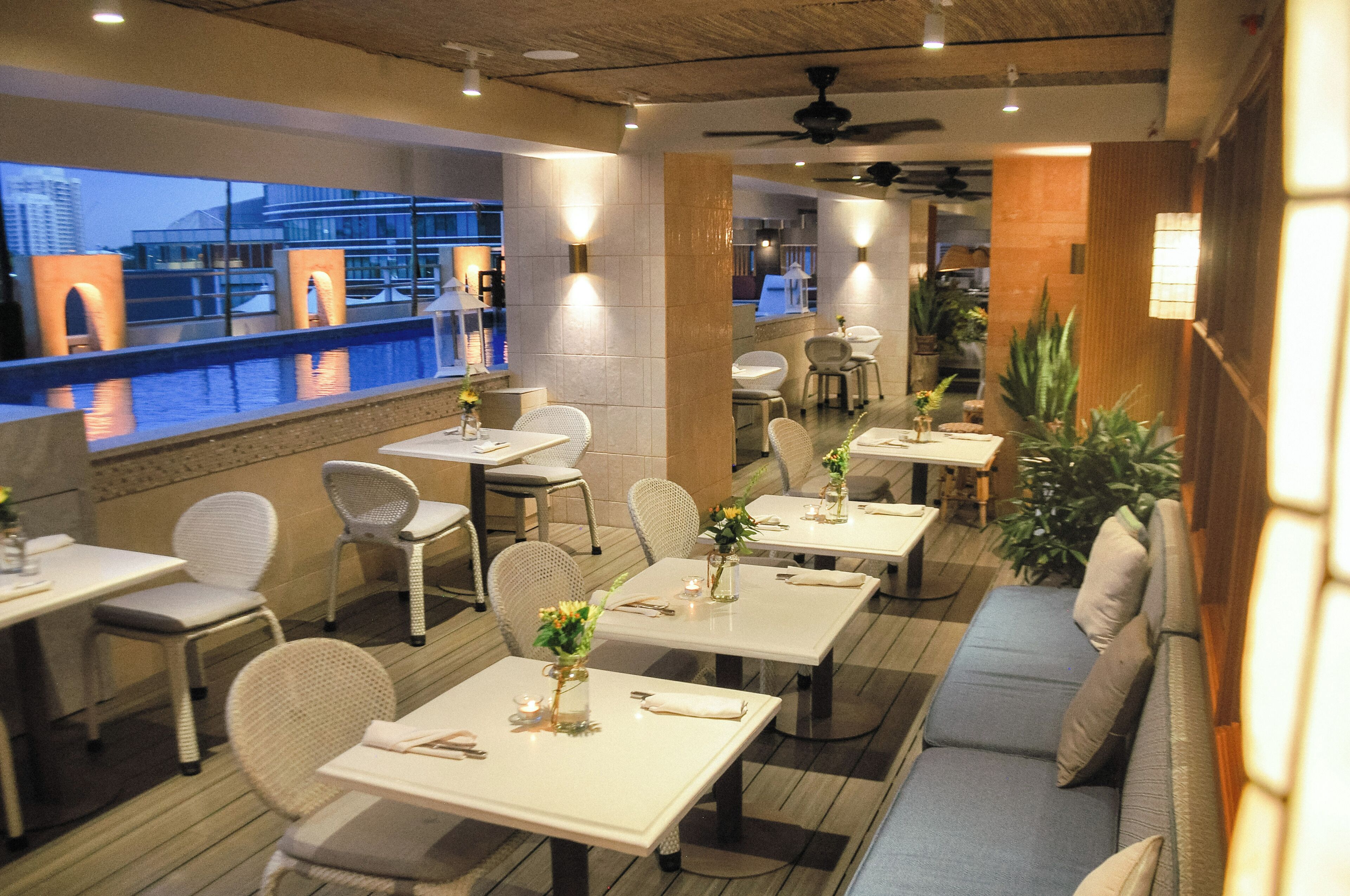 Ein Restaurant mit Außenbereich, Tischen mit weißen Tischdecken und Blick auf ein Gebäude gegenüber dem Wasser.