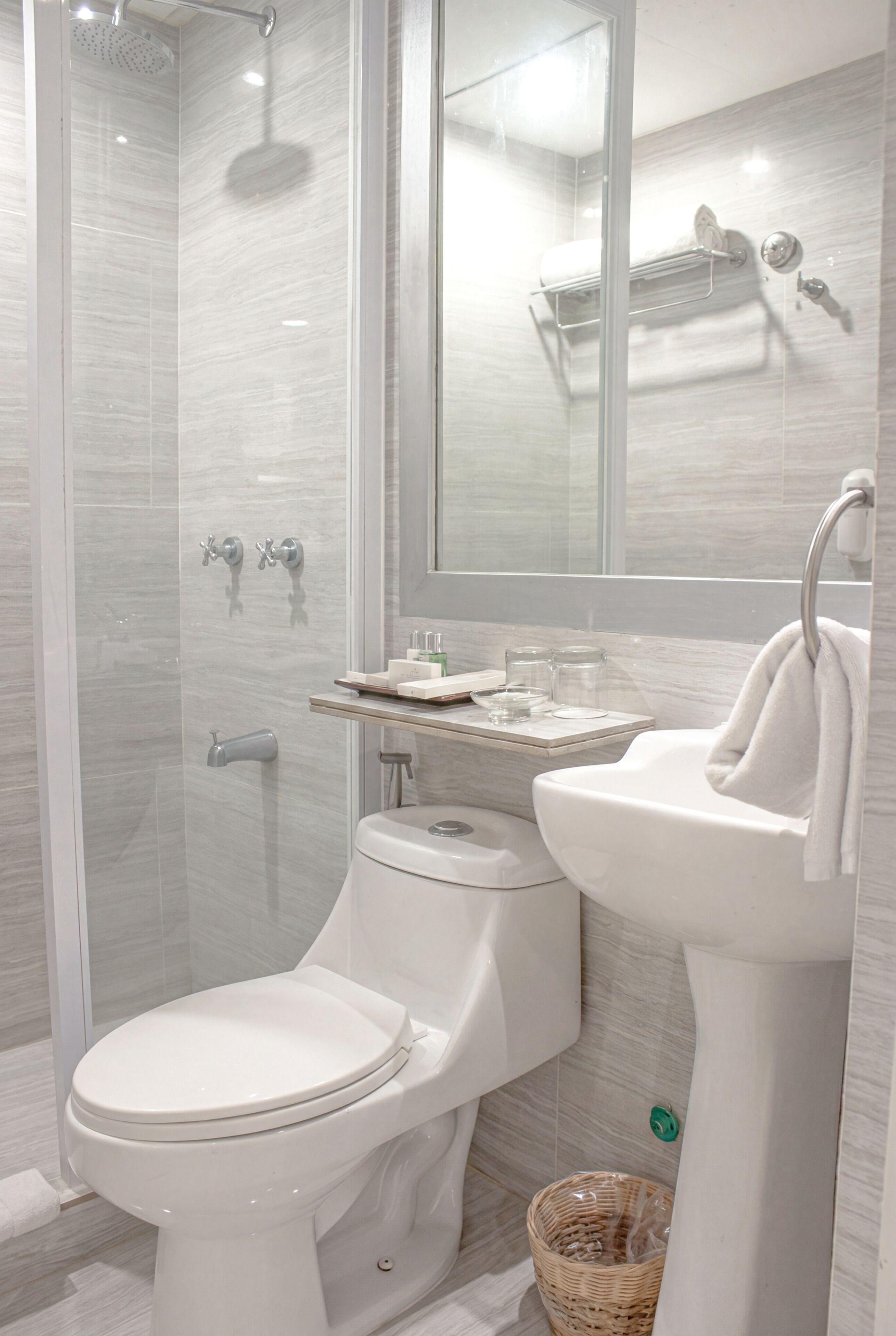 Une salle de bain moderne avec une douche à parois de verre, des toilettes blanches, un lavabo avec un porte-serviettes et un miroir au-dessus du lavabo.
