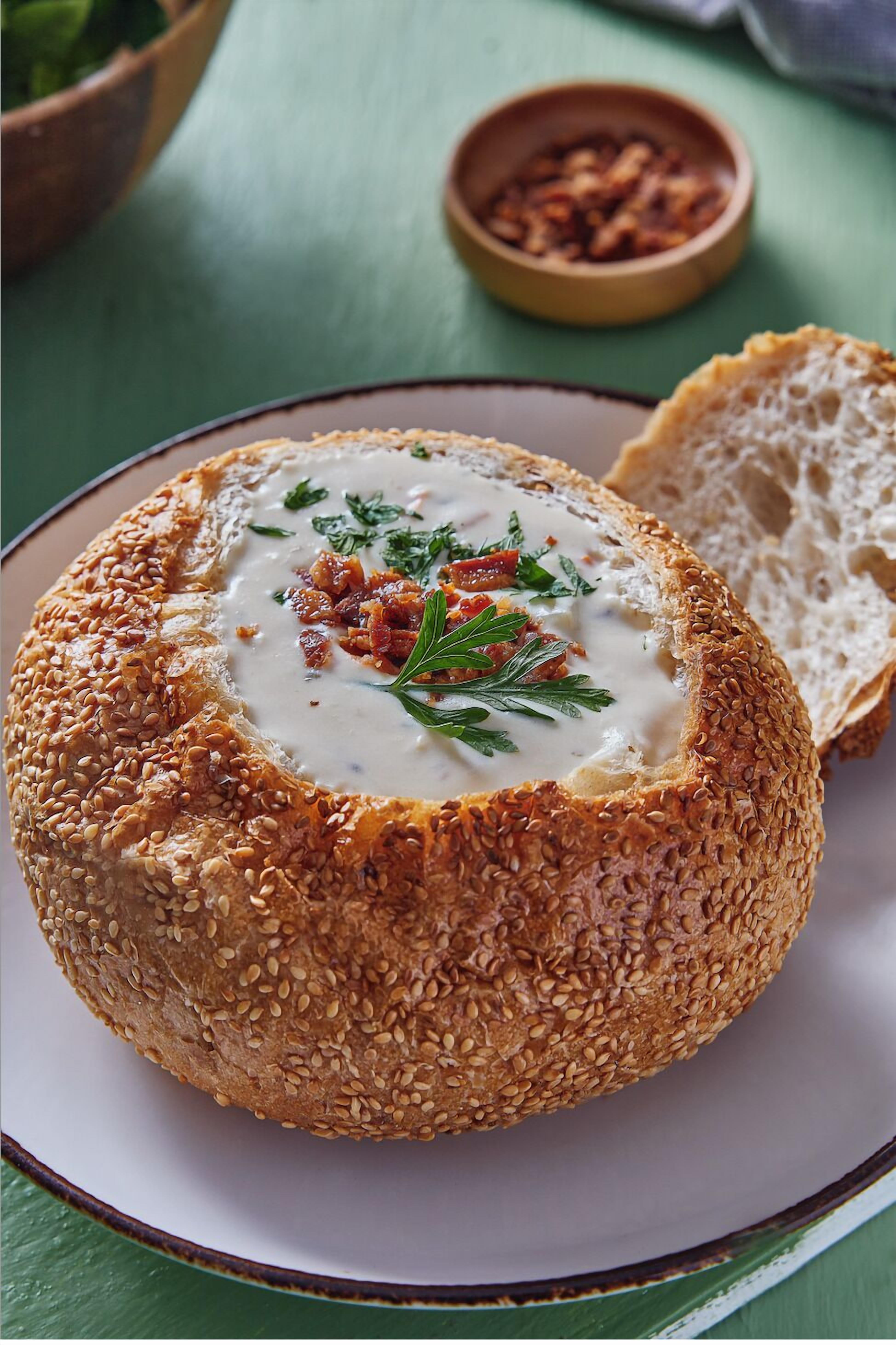 A round bread with sesame seeds and a creamy topping, accompanied by a slice of bread on a plate.