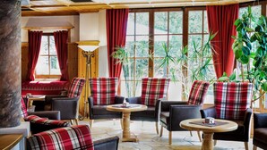 A cozy lounge area with plaid-patterned chairs, a wooden coffee table, and a large window with red curtains. - Hotel Appartement Similaun (Soelden)