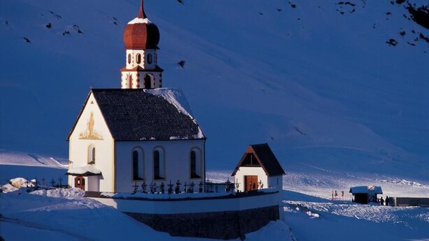 A church with a red dome and a bell tower, surrounded by snow-covered ground and a clear sky. - Hotel Appartement Similaun (Soelden)