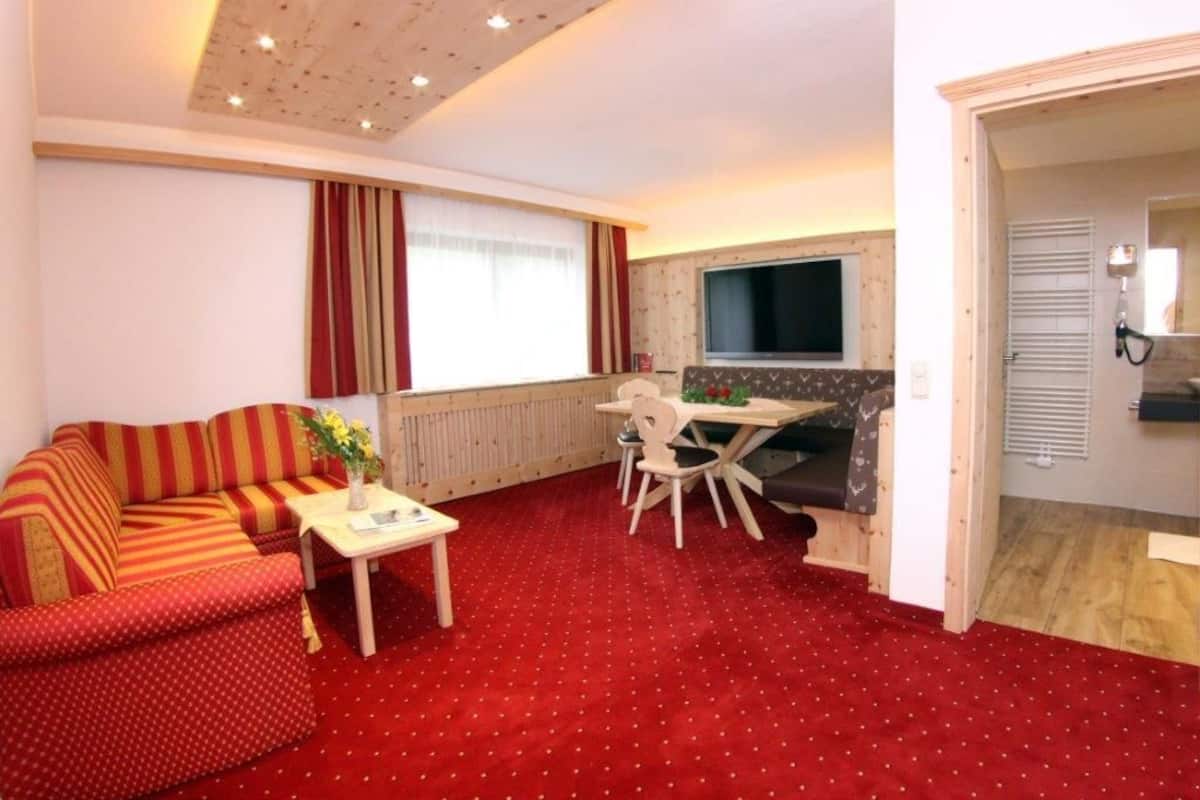 Ein gemütliches Wohnzimmer mit rotem Teppich, einer Couch, einem Esstisch mit Stühlen, einem Fernseher und einem Kamin.