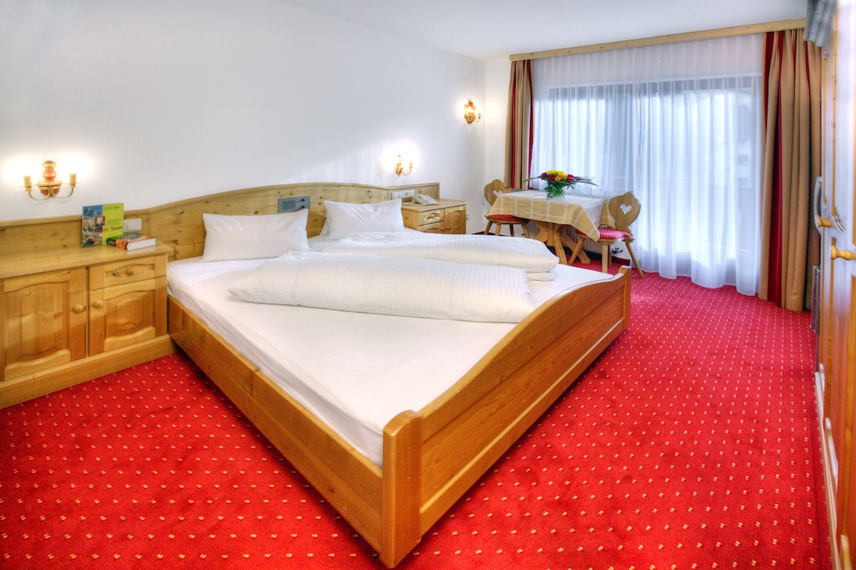 Ein Hotelzimmer mit einem großen Bett, einem Holz-Kopfteil, einem Schreibtisch mit Stuhl und einem kleinen Tisch mit Blumen.