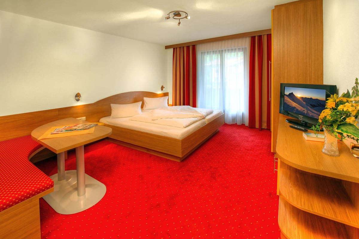 Ein Hotelzimmer mit Bett, kleinem Tisch mit einer Zeitschrift, Fernseher und Schreibtisch mit Blumenvase.