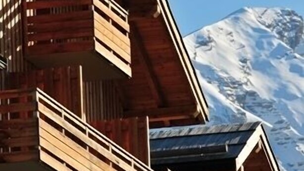 Una cabaña de madera con balcones, con una imponente montaña nevada al fondo.