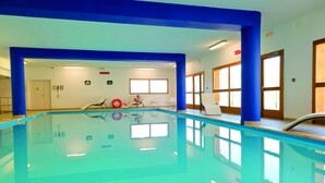 Una piscina interior con agua azul cristalina, rodeada de columnas azules y paredes blancas.