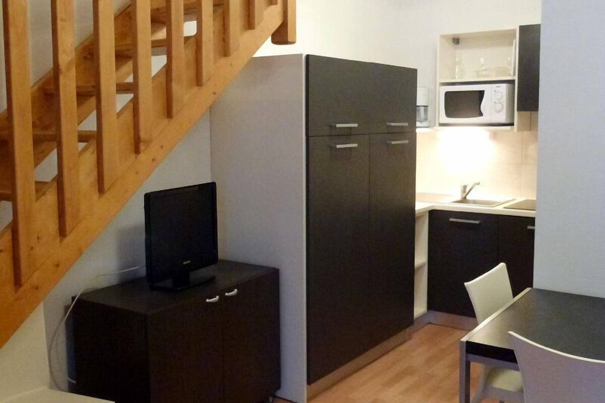 Cuina compacta amb microones, nevera petita i zona de menjador amb una cadira.