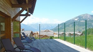 Terraza de madera con sillones, vista a las montañas y una cerca verde.