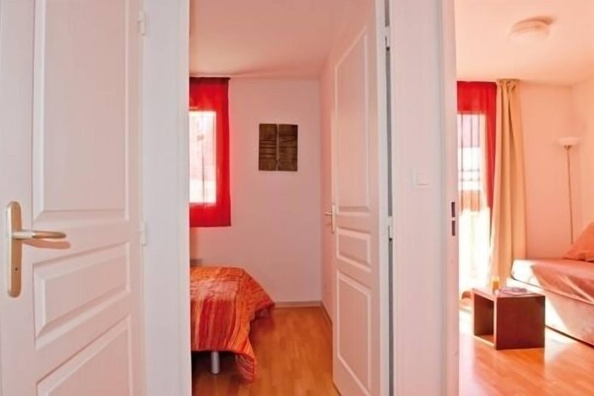 Una habitació amb un llit, una taula petita i una porta que dona a una altra habitació.