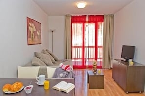 Ein gemütliches Wohnzimmer mit einer Couch, einem Couchtisch mit Gebäck, einem Fernseher und einem Bücherregal.