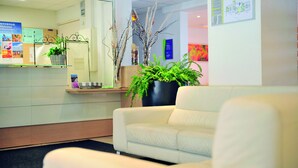 Un área de recepción con un sofá blanco, una planta y un tablón de anuncios con carteles de bienvenida.