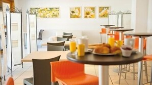 Un comedor moderno con mesas y sillas, alimentos para el desayuno sobre una mesa y una obra de arte floral en la pared.
