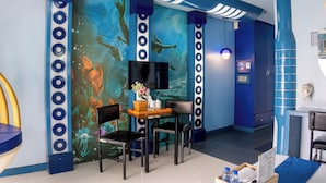 Una habitación con un mural de escenas submarinas, una mesa con sillas, un televisor de pantalla plana y un mueble bajo.