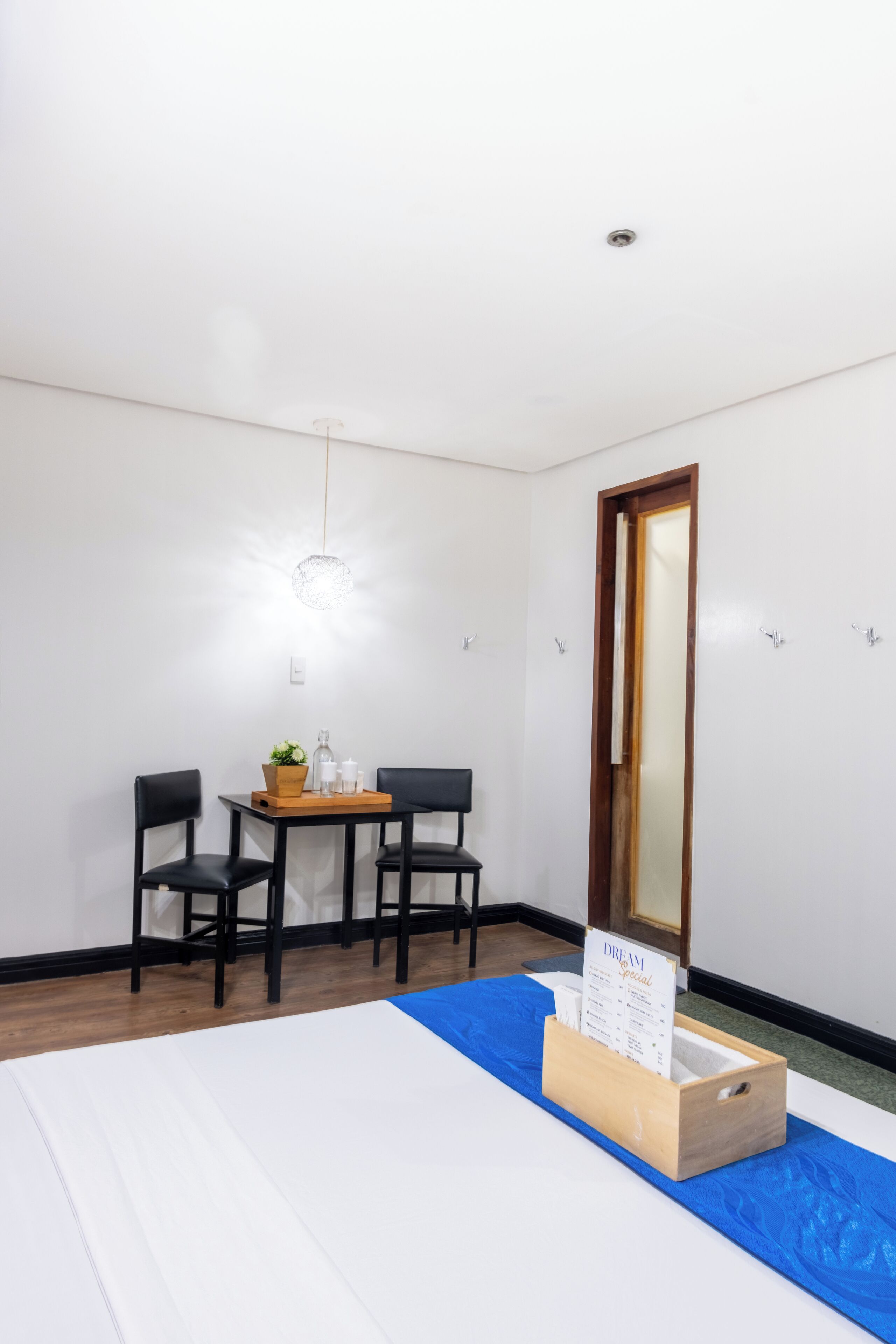A hotel room with a bed, a desk with two chairs, a mirror, and a sign on the desk.