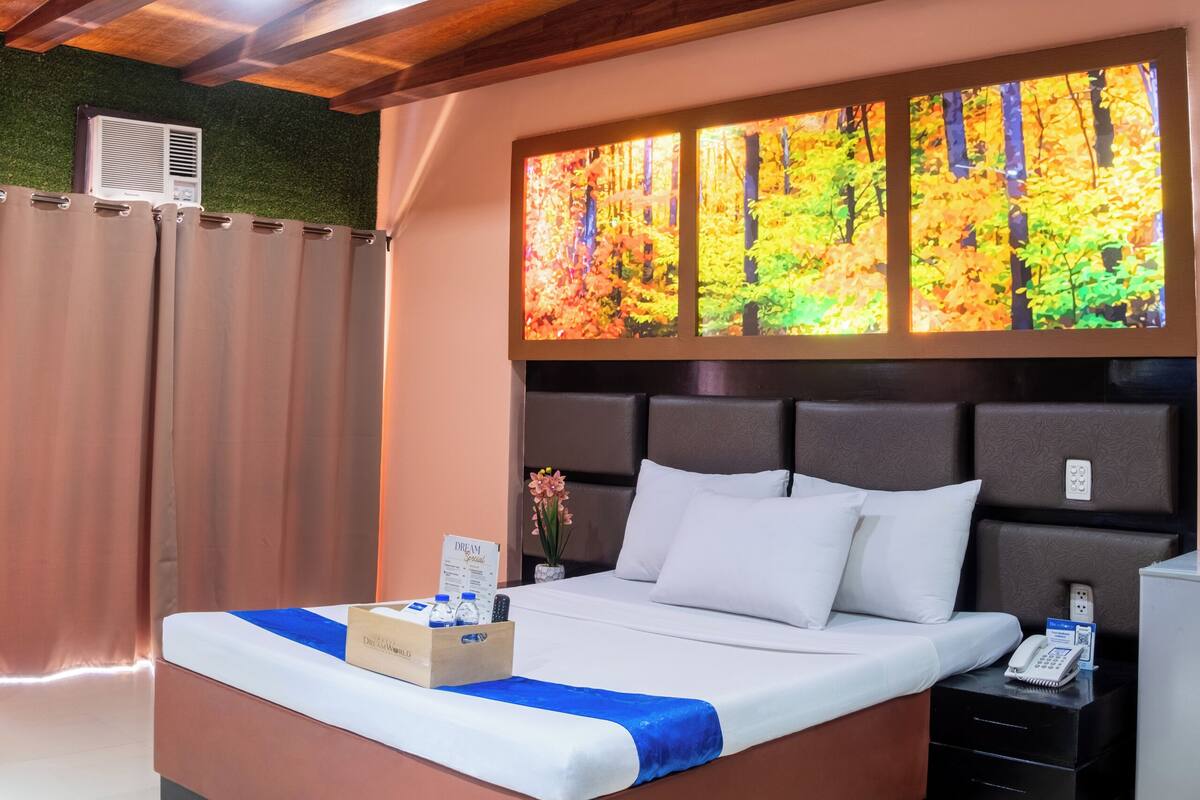 Habitación de hotel con una cama grande, una mesita de noche, un televisor montado en la pared y un techo con vigas de madera.