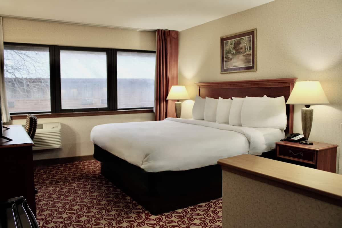 A hotel room with a large bed, two bedside tables with lamps, a desk, and a window with a view.