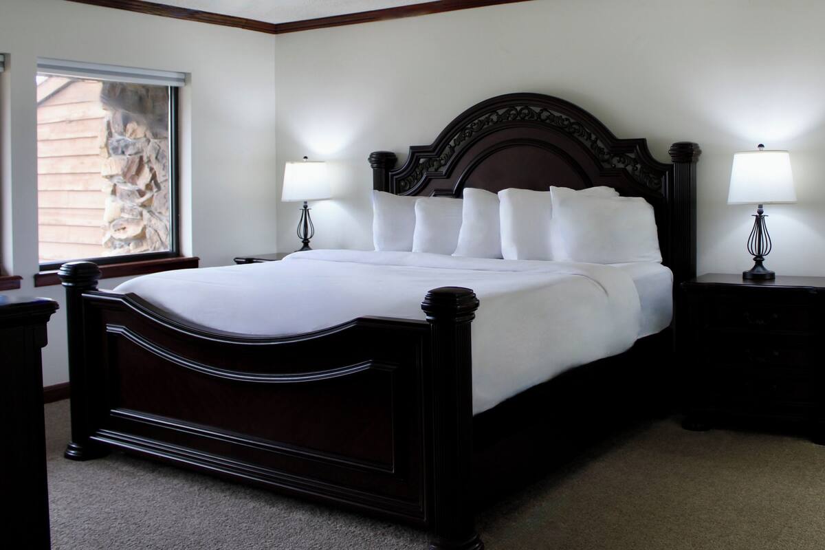 A neatly made bed with white linens, two bedside tables with lamps, and a window with a stone facade view.