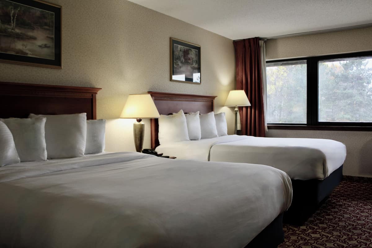 A hotel room with two beds, a large window with a view of trees, and a painting on the wall.