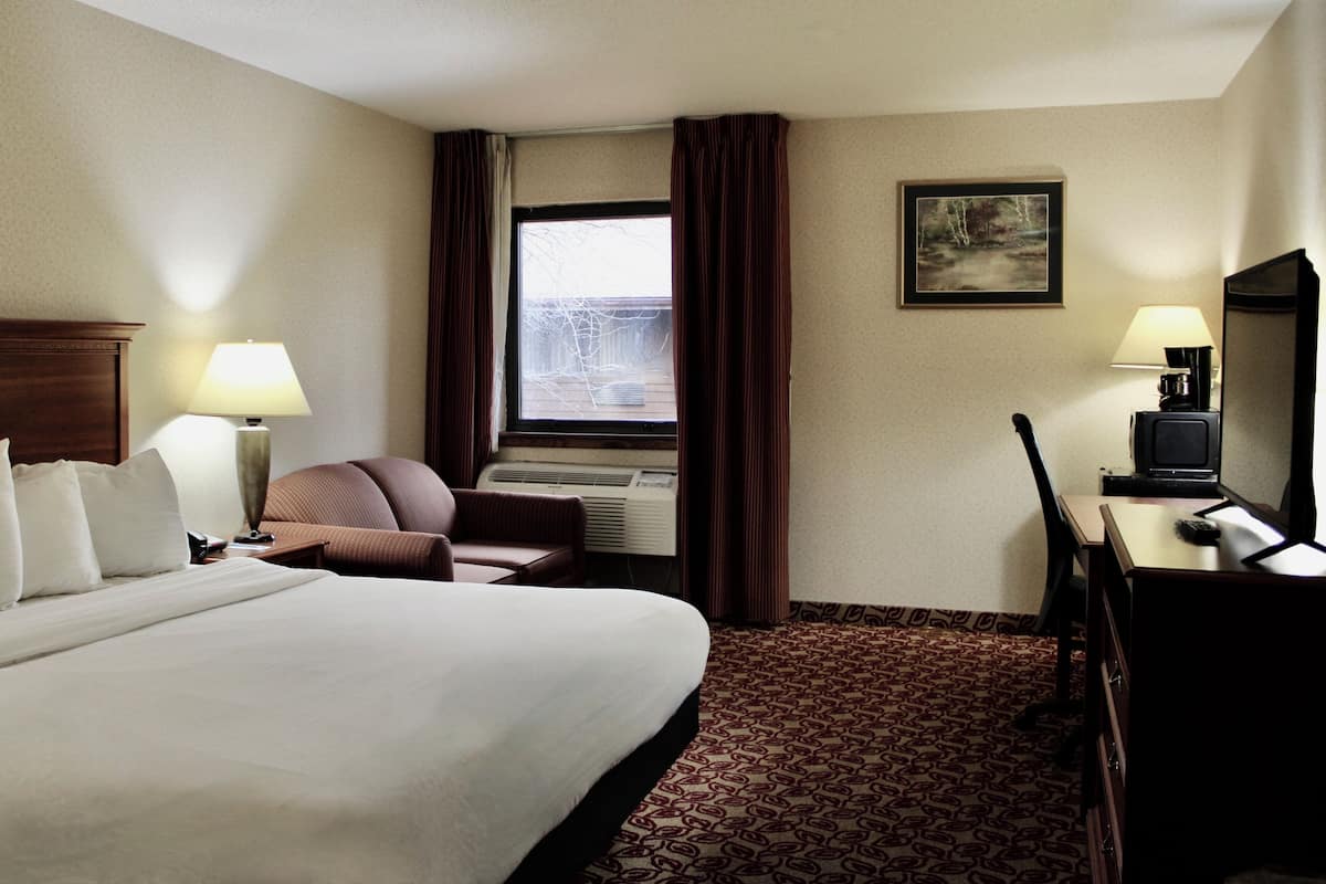 A hotel room with a large bed, a desk, a chair, a TV, and a window with curtains.